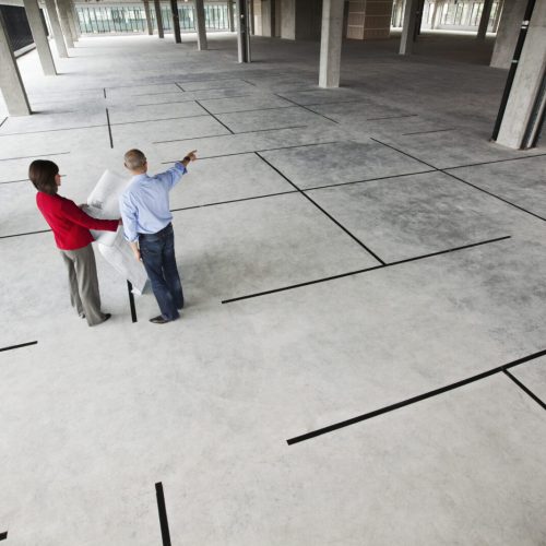 Asian architect with caucasian woman planning workspaces in a new raw office location Asian architect with caucasian woman planning workspaces in a new raw office location