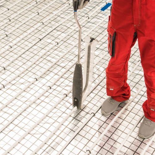 Worker Using Floor Radiant Heating Pipeline Foam Board Stapler Caucasian HVAC Worker Using Floor Radiant Heating Pipeline Foam Board Stapler Attaching Plastic Pipe to Foam Using Staples. Residential Heating Systems.